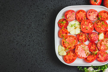 Tomato slices in a baking dish with garlic and thyme. Top view, space for text.