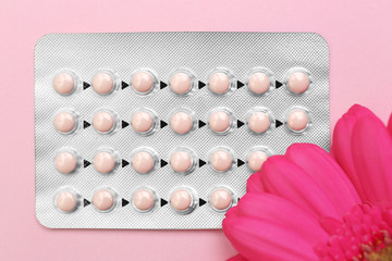 Blister of contraceptive pills with flower on color background