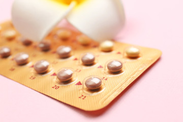 Blister of contraceptive pills with flower on color background