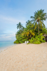 Maldives. Tropical island. Indian Ocean. Maldives. White sand beach, palm trees above the water. Two chaise lounges for rest.