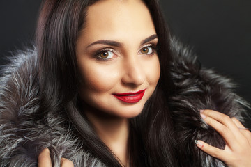 Obraz premium Beautiful woman with clean fresh skin. In winter fur coat. Beautiful smile. Red lipstick On a black background.