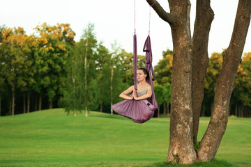 Young woman practicing aerial yoga on tree in park © Africa Studio