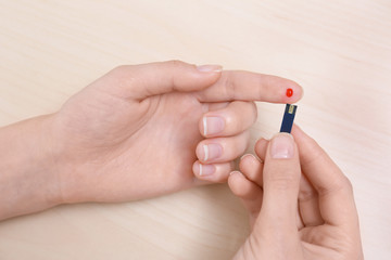 Woman using test strip for glucose level on wooden background