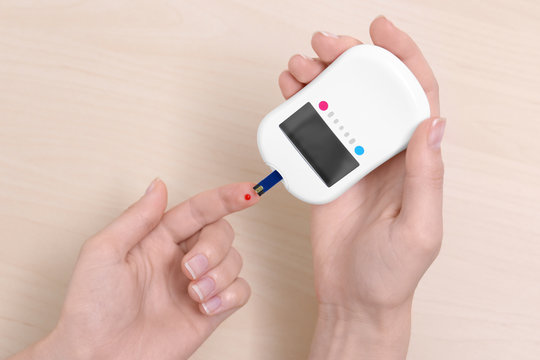 Woman testing glucose level with digital glucometer on wooden background