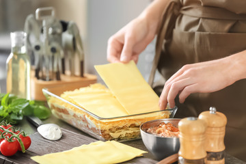 Woman preparing meat lasagna in kitchen