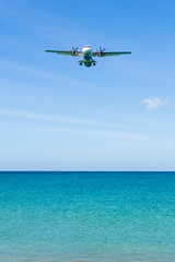 Obraz na płótnie Canvas Airplane landing above beautiful beach and sea background