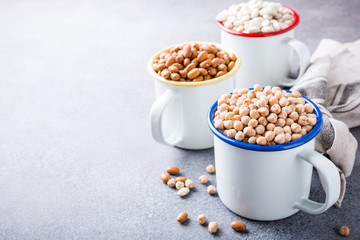 Raw uncooked organic chickpeas and kidney beans in white enamel mugs on rustic wooden board on light gray stone background. Healthy vegan vegetarian food concept with copy space.
