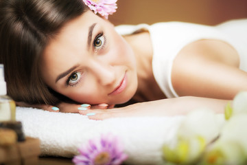 Obraz na płótnie Canvas Massage. Beautiful woman at the spa. Gentle look. Flowers in hair. The concept of health and beauty. Dark background. Spa salon.