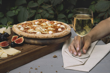 Pizza on board, cheese, bread. Woman holds a glass of wine