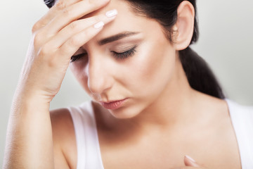 Naklejka premium Portrait of a beautiful young brunette with bare shoulders, severe headaches, migraine, colds. The concept of treatment. Holds his hand to his forehead.
