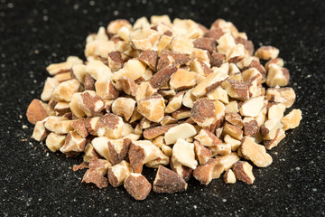 Pile of chopped roasted almond pieces on a black background