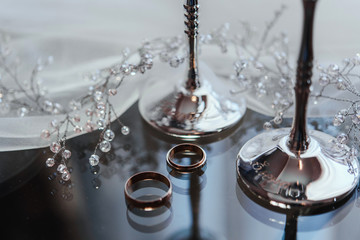 два золотых обручальных кольца со свадебными бокалами на стеклянном фоне © oes