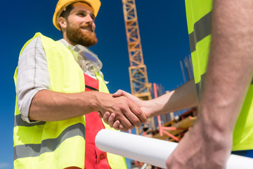 Bauarbeiter auf Baustelle mit Bauplan finden Vereinbarung und Handschlag