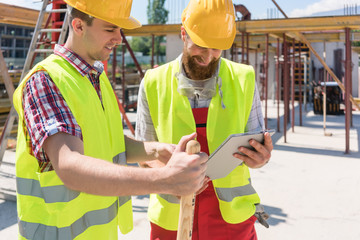 Bauarbeiter sehen sich Baupläne auf Tablet Computer auf der Baustelle an