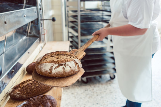 B&auml;cker Frau in Backstube legt Brot auf Brett ab
