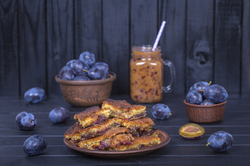 Homemade plum pie in plate, plum smoothies and raw plums on black wooden background