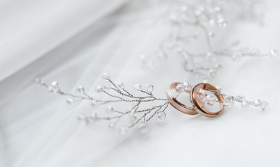 два золотых обручальных кольца со свадебными украшениями невесты на белом фоне © oes