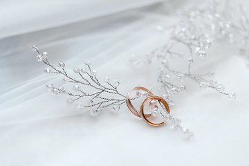 два золотых обручальных кольца со свадебными украшениями невесты на белом фоне