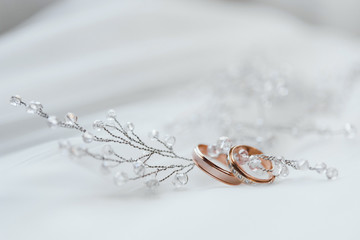 два золотых обручальных кольца со свадебными украшениями невесты на белом фоне © oes