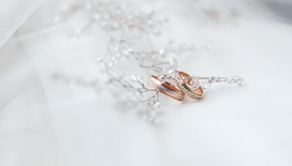 два золотых обручальных кольца со свадебными украшениями невесты на белом фоне © oes