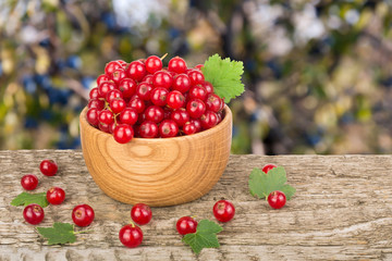 Red currant berries in wooden bowl on wooden table with blurry garden background