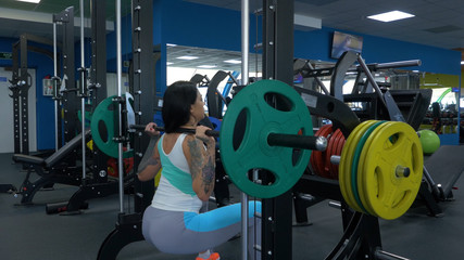Plakat Beautiful girl exercising squatting with barbell. Sportive woman doing squatting with a barbell at the gym. Fit woman doing squat with barbell in the gym closeup