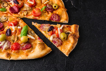 Cut into slices delicious fresh pizza with mushrooms and pepperoni on a dark background. Top view . Pizza on the black table. 