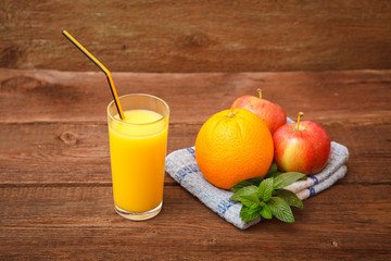 A glass of a glass of refreshing orange juice on a wooden background. Orange, apples, melissa and fruit juice. Space for text.