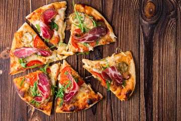 Homemade pizza with tomatoes, cheese, meat and herbs. Pizza on a wooden background. Restaurant meal. Copy space.