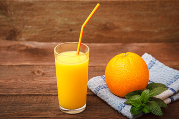 Freshly squeezed orange juice in a glass with a straw and fresh orange with mint, melissa on a wooden background. Space for text. Background.