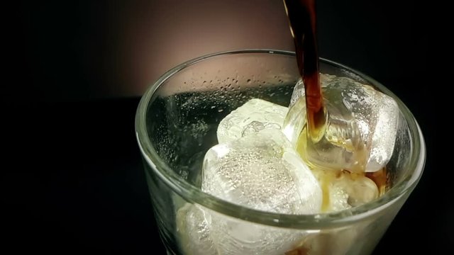 pouring of fresh coke in the drink glass with ice cubes on black background, fun and summer time concept