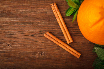 Fresh orange with cinnamon, mint and melissa on a wooden background. Close-up. Top view. Space for text. Background