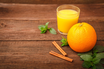 A glass of a glass of refreshing orange juice on a wooden background. Orange,  melissa, cinnamon and fruit juice. Space for text.