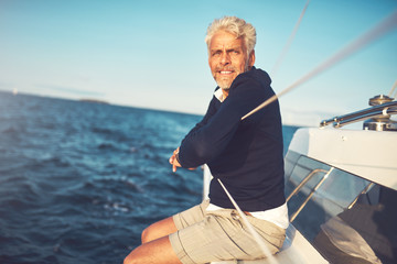 Fototapeta premium Mature man sitting on his sailboat looking at the ocean