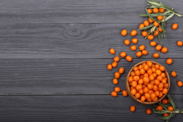Obraz na płótnie Canvas Sea buckthorn. Ripe fresh berries in bowl on black wooden background with copy space for your text. Top view