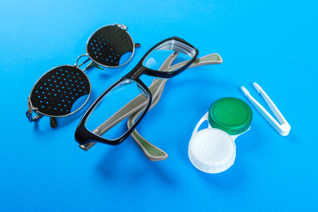 A set of accessories for sight. Pinhole glasses, lenses with container and glasses for sight. Pair of medical pinhole glasses with reflections. Medical concept. Top view.