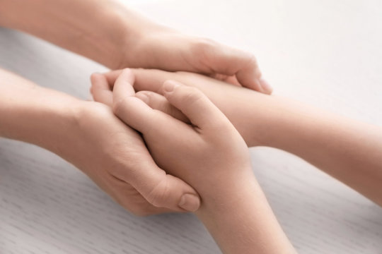 Mother and daughter holding hands together on light background, closeup