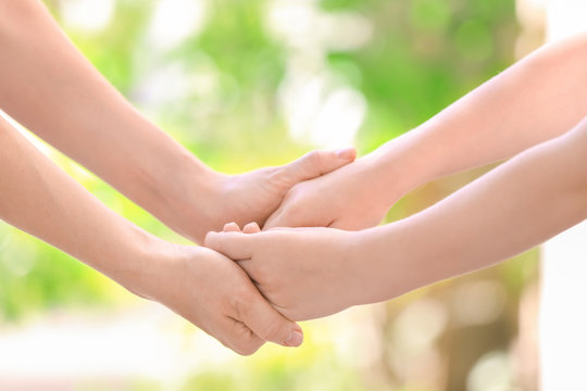 Mother and daughter holding hands together on blurred background, closeup