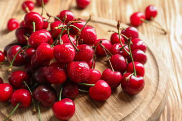 Wooden board with tasty ripe cherries on table