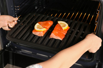 Woman putting baking tray with slices of red fish fillet into oven