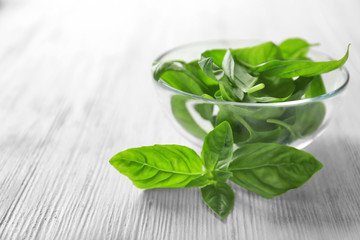 Green fresh organic basil leaves in glass bowl on wooden background