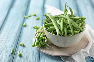 Bowl and fresh green beans on wooden background