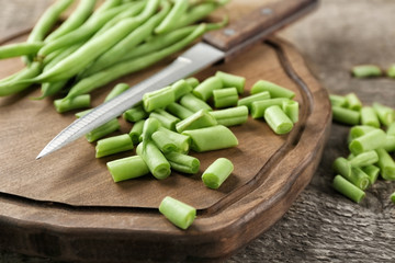 Wooden board with fresh green beans on table