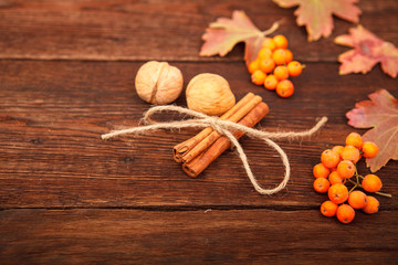 Autumn concept. Red-yellow leaves, berries of mountain ash, walnut and cinnamon on a wooden background. Space for text.