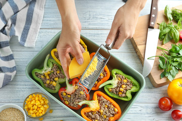 Woman adding cheese to quinoa stuffed peppers in kitchen