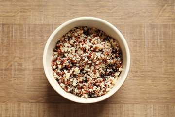 Bowl with boiled quinoa grains on wooden table