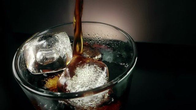 top of view pouring of fresh coke in the drink glass with ice cubes on black background, fun and summer time concept