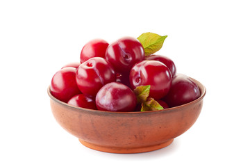 Ripe red plums in ceramic bowl on white