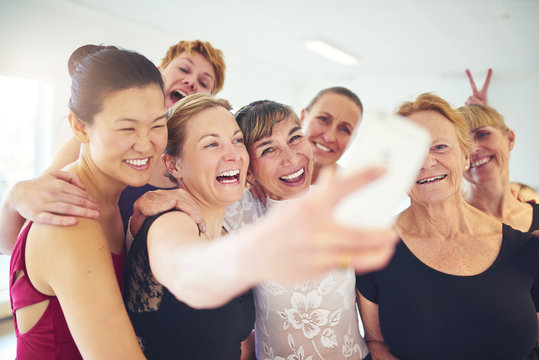 Group of laughing friends taking selfies in a dance studio
