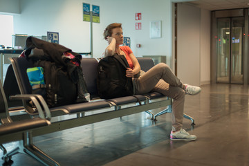 Fototapeta na wymiar Young woman with luggage waiting in the airport hall her plane